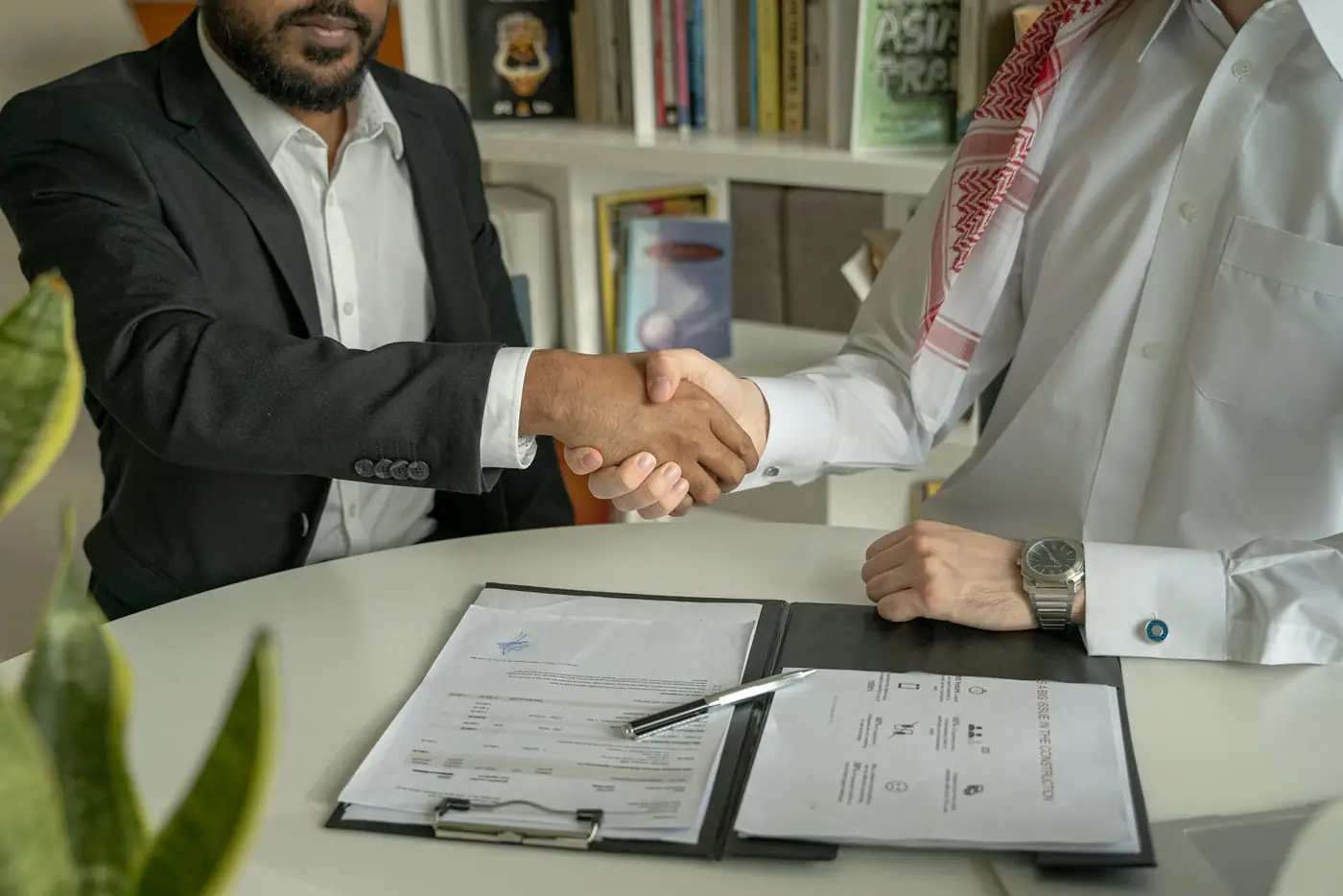 Business partners shaking hands over signed documents